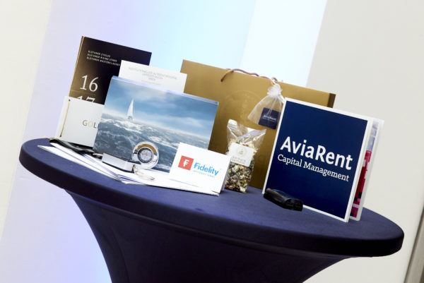 Goodie Bag 2016 nebst Informationsunterlagen von Fidelity, Pimco, AviaRent und LMM Investment Controlling fanden die Teilnehmer darin eine Pimco-Kofferwaage, eine exklusive Fidelity-Power Bank, einen LMM-Kompass, einen Gutschein von Blüthner für 2 Konzertkarten, einen AviaRent-USB-Stick sowie Barbara Bertolini-Popcorn in verschiedenen Sorten